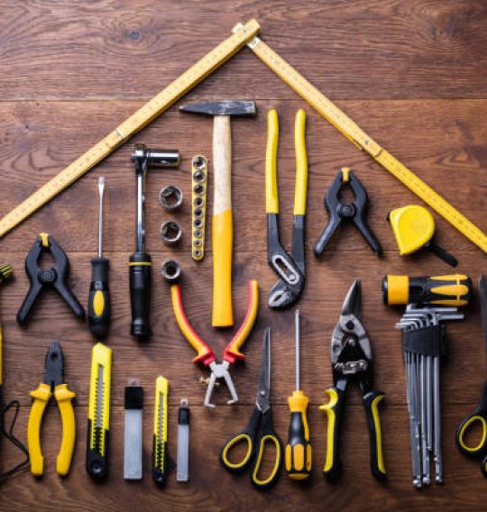 istockphoto-949187600-612×612 Elevated View Of Many Tools With Roof Made With Yellow Measuring Tape On Wooden Table